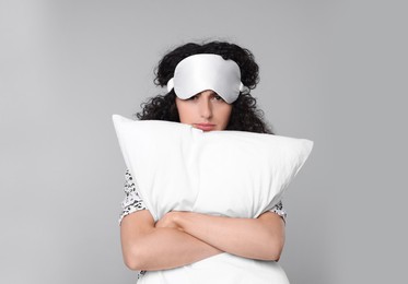 Tired young woman with sleep mask and pillow on light grey background. Insomnia problem