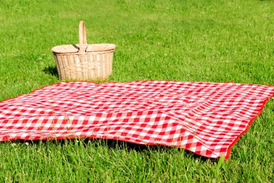 Photo of Checkered tablecloth and picnic basket on green grass