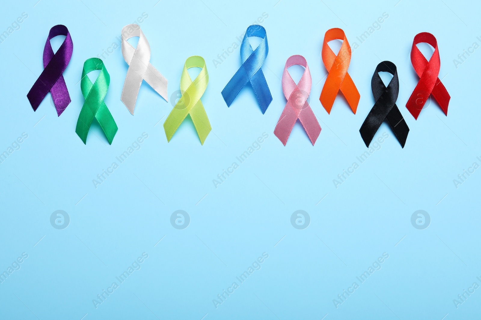 Photo of Colorful ribbons on light blue background, flat lay with space for text. World Cancer Day