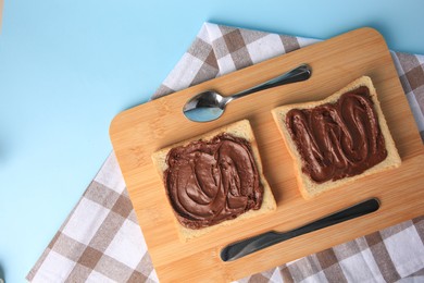 Photo of Tasty toasts with chocolate paste served on light blue background, top view. Space for text