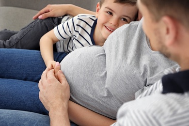 Photo of Pregnant mother, father and son spending time together on sofa at home. Family time