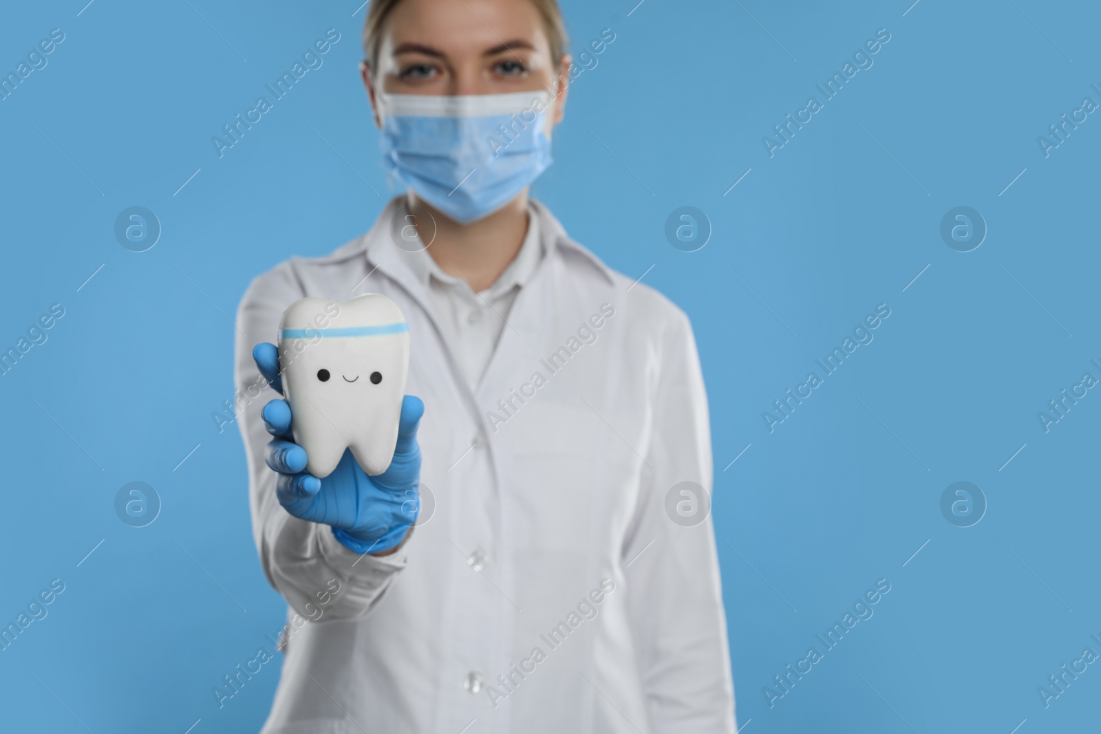 Photo of Dental assistant holding toy tooth with funny face against light blue background, focus on hand. Space for text