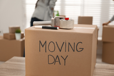 Photo of Cardboard box with words MOVING DAY and packaging items on wooden table