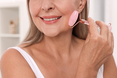 Photo of Woman massaging her face with rose quartz roller in bathroom, closeup