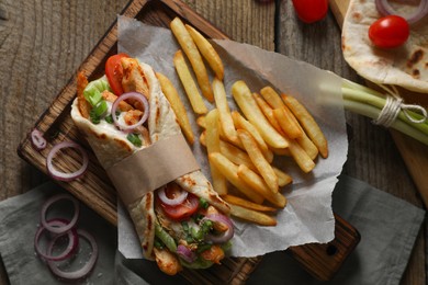 Photo of Delicious pita wrap with meat, vegetables and potato fries on wooden table, flat lay