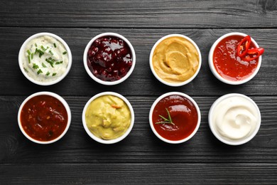 Different tasty sauces in bowls on black wooden table, flat lay