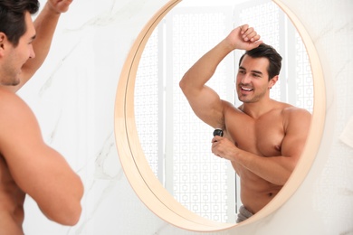 Handsome young man applying deodorant in bathroom