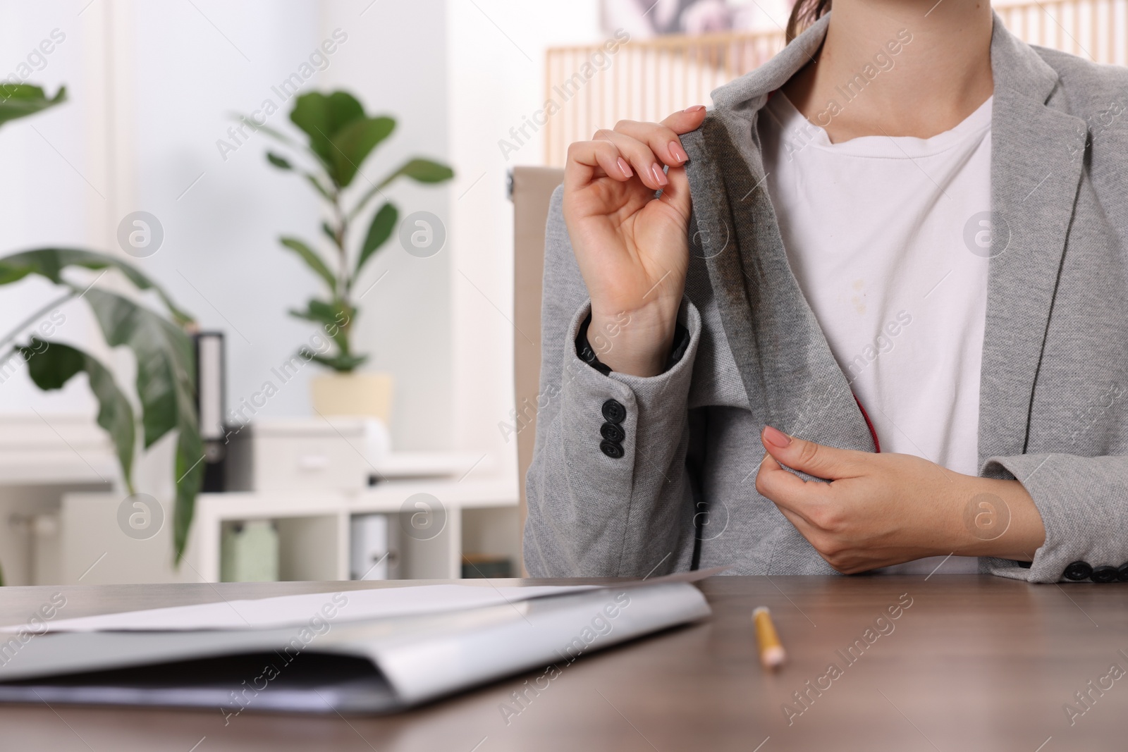 Photo of Woman showing stain from coffee on her jacket at wooden table indoors, closeup