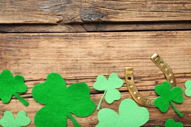 Photo of Decorative clover leaves and horseshoe on wooden background, flat lay with space for text. St. Patrick's Day celebration