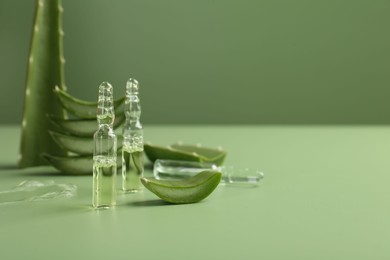 Skincare ampoules with extract of aloe vera and cut green leaves on color background. Space for text