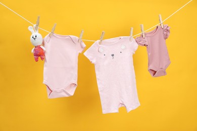 Photo of Different baby clothes and bunny toy drying on laundry line against orange background