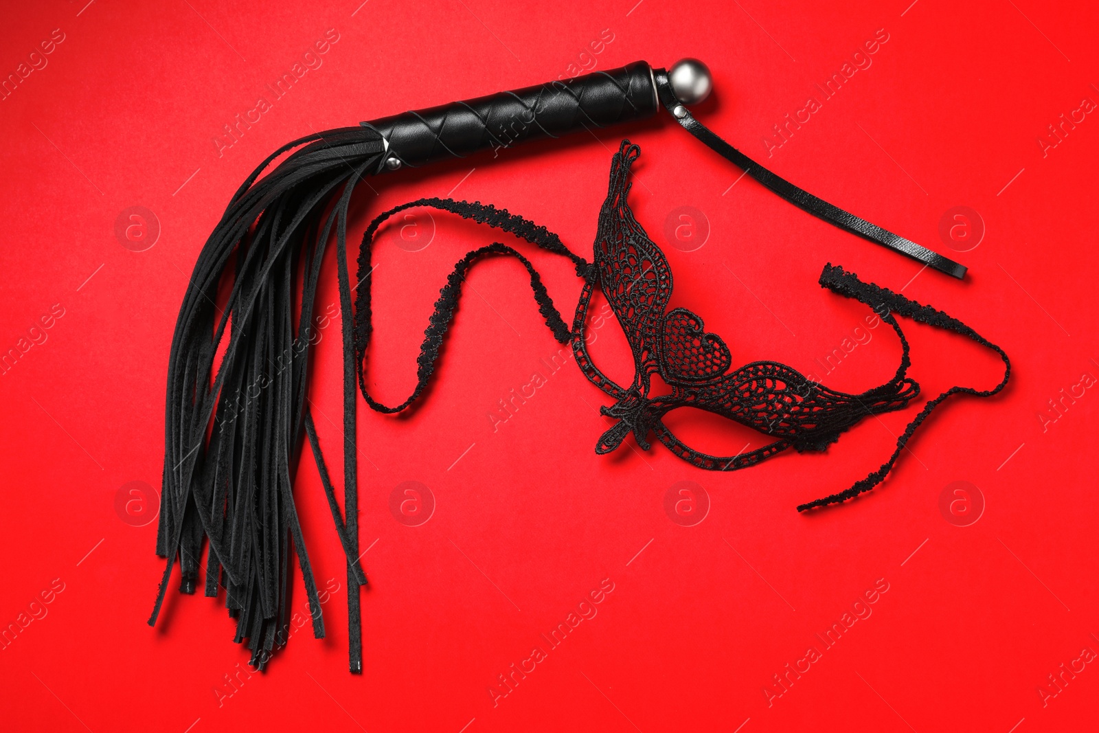 Photo of Black whip and lace mask on ed background, flat lay. Accessories for sexual role play