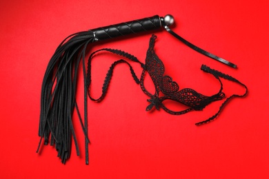 Photo of Black whip and lace mask on ed background, flat lay. Accessories for sexual role play