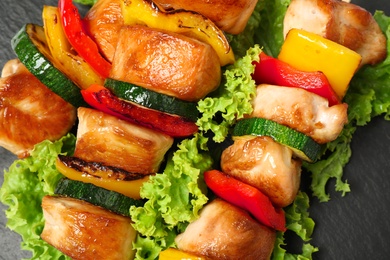 Photo of Delicious chicken shish kebabs with vegetables on black table, closeup