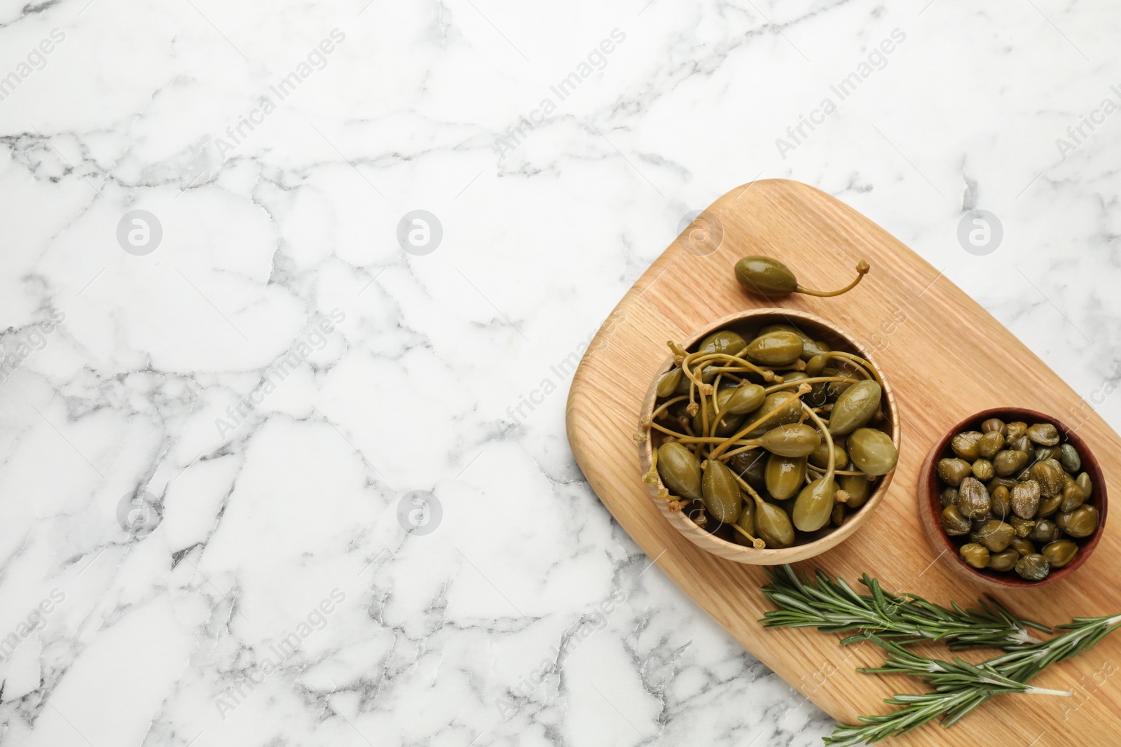 Photo of Delicious pickled capers and rosemary twigs on white marble table, top view. Space for text