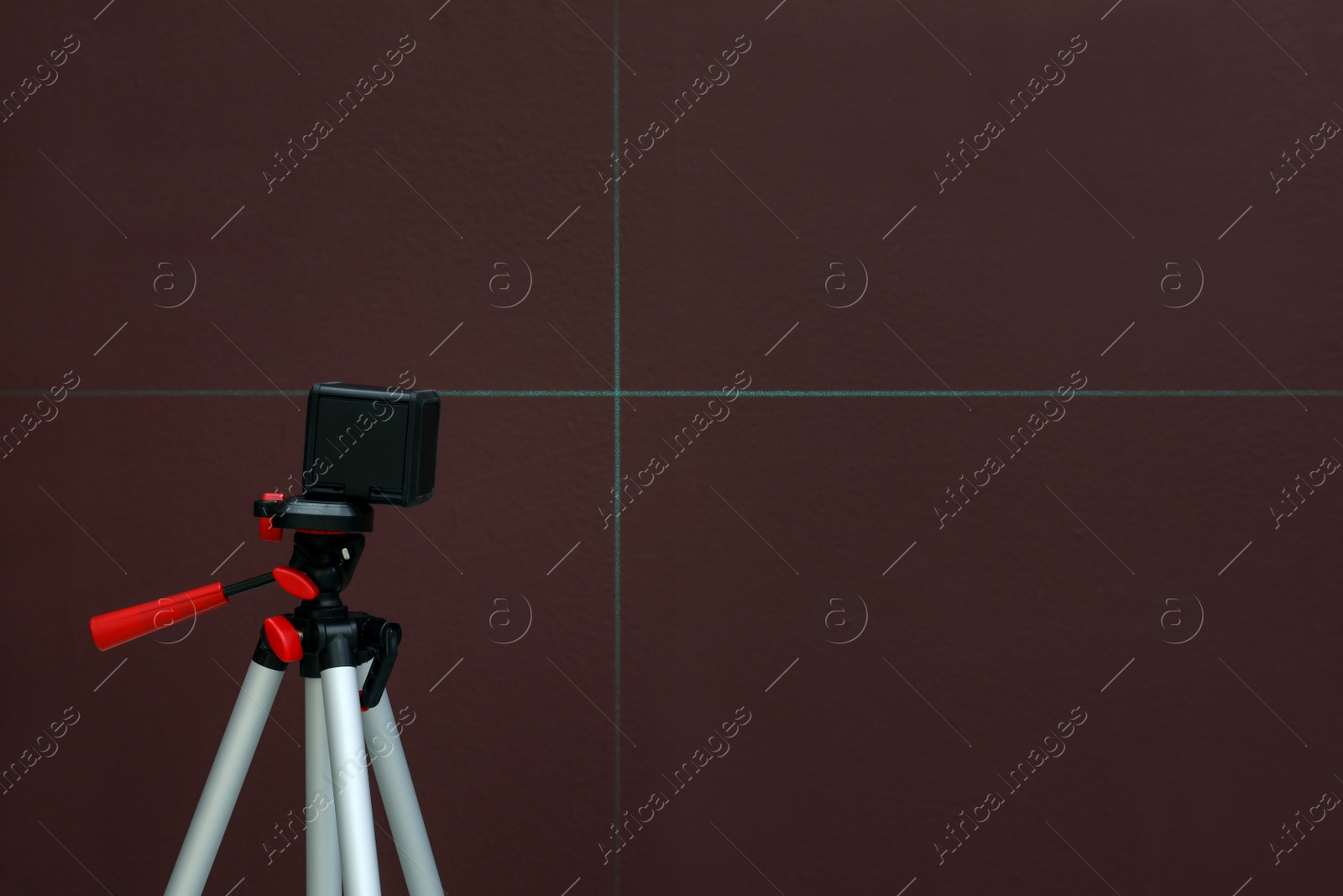 Photo of Cross line laser level on tripod in front of brown wall