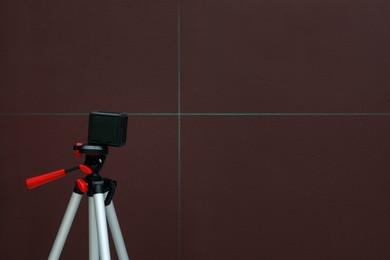 Photo of Cross line laser level on tripod in front of brown wall