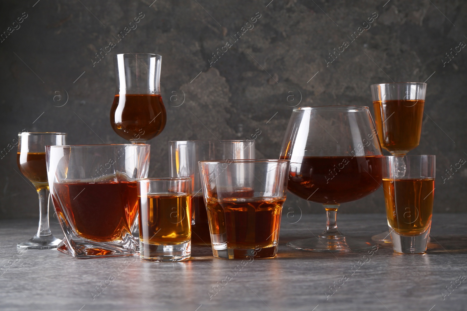 Photo of Many different liqueurs in glasses on grey textured table