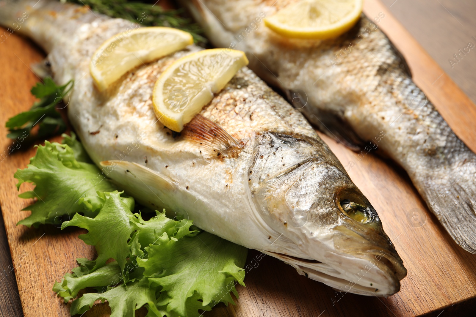 Photo of Delicious baked fish, lettuce and lemon on wooden board, closeup