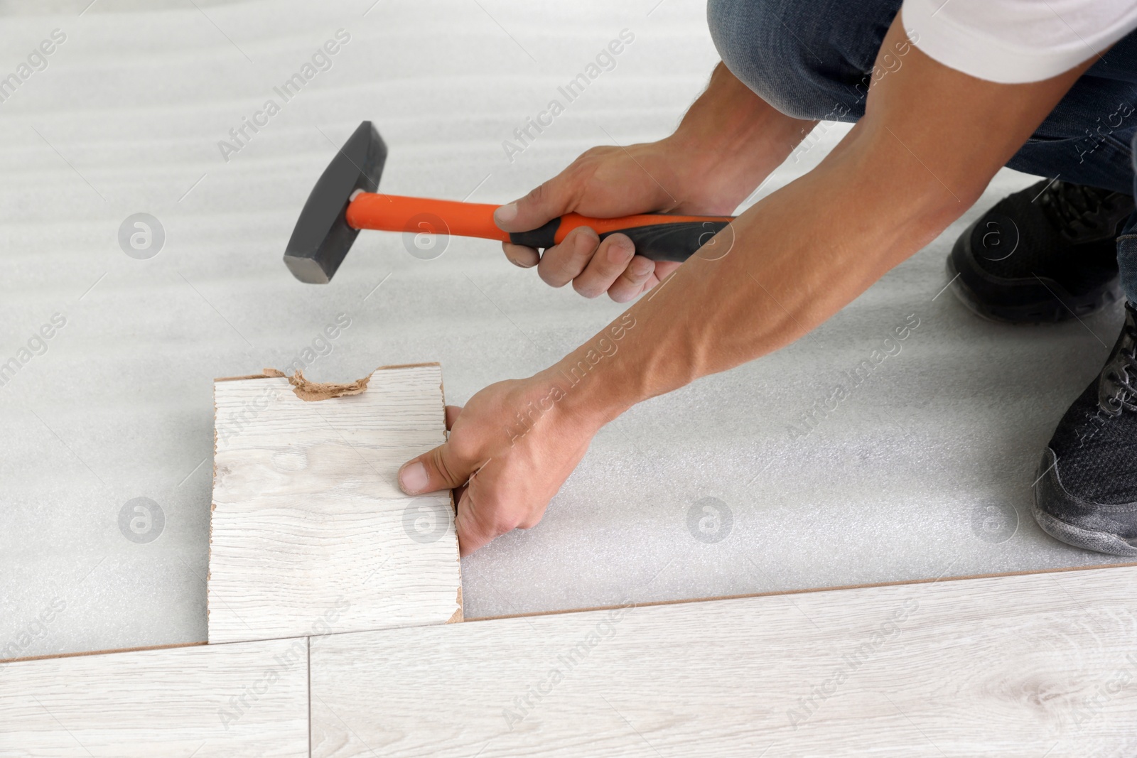 Photo of Man using hammer during installation of new laminate flooring, closeup