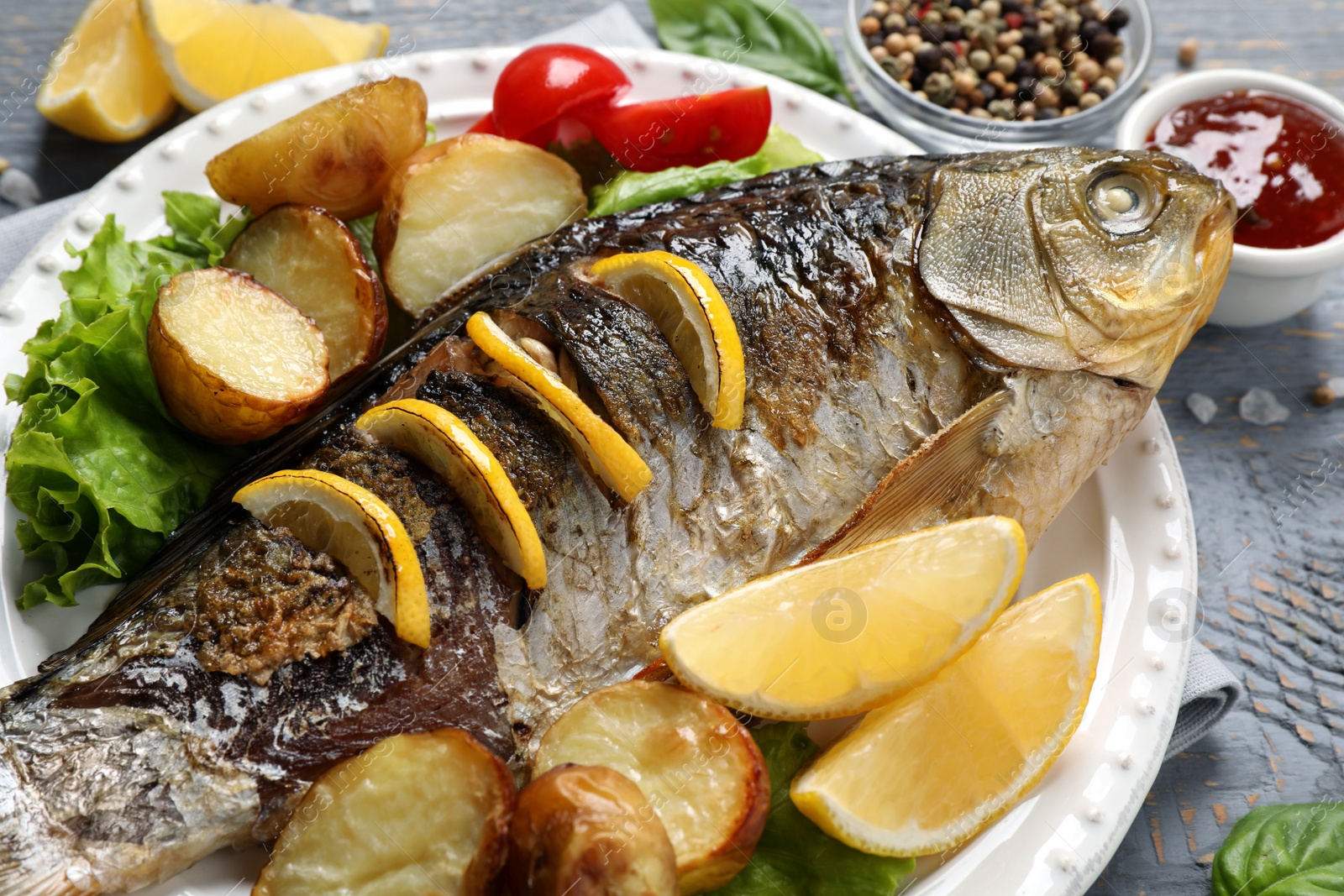 Photo of Tasty homemade roasted crucian carp served on grey wooden table, closeup. River fish