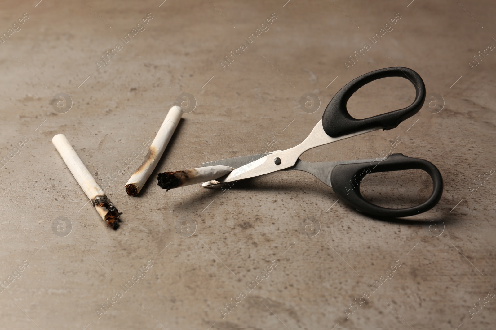 Photo of Scissors cutting burnt cigarettes on grey textured table. No smoking concept