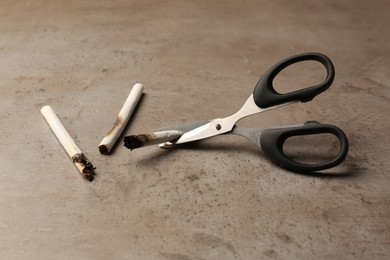 Scissors cutting burnt cigarettes on grey textured table. No smoking concept