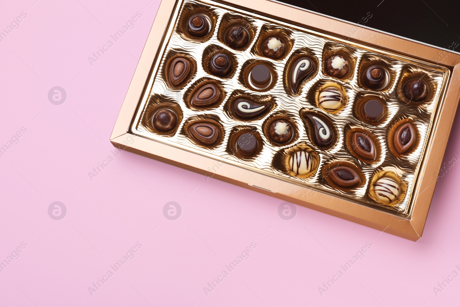 Photo of Box of delicious chocolate candies on pink background, top view. Space for text