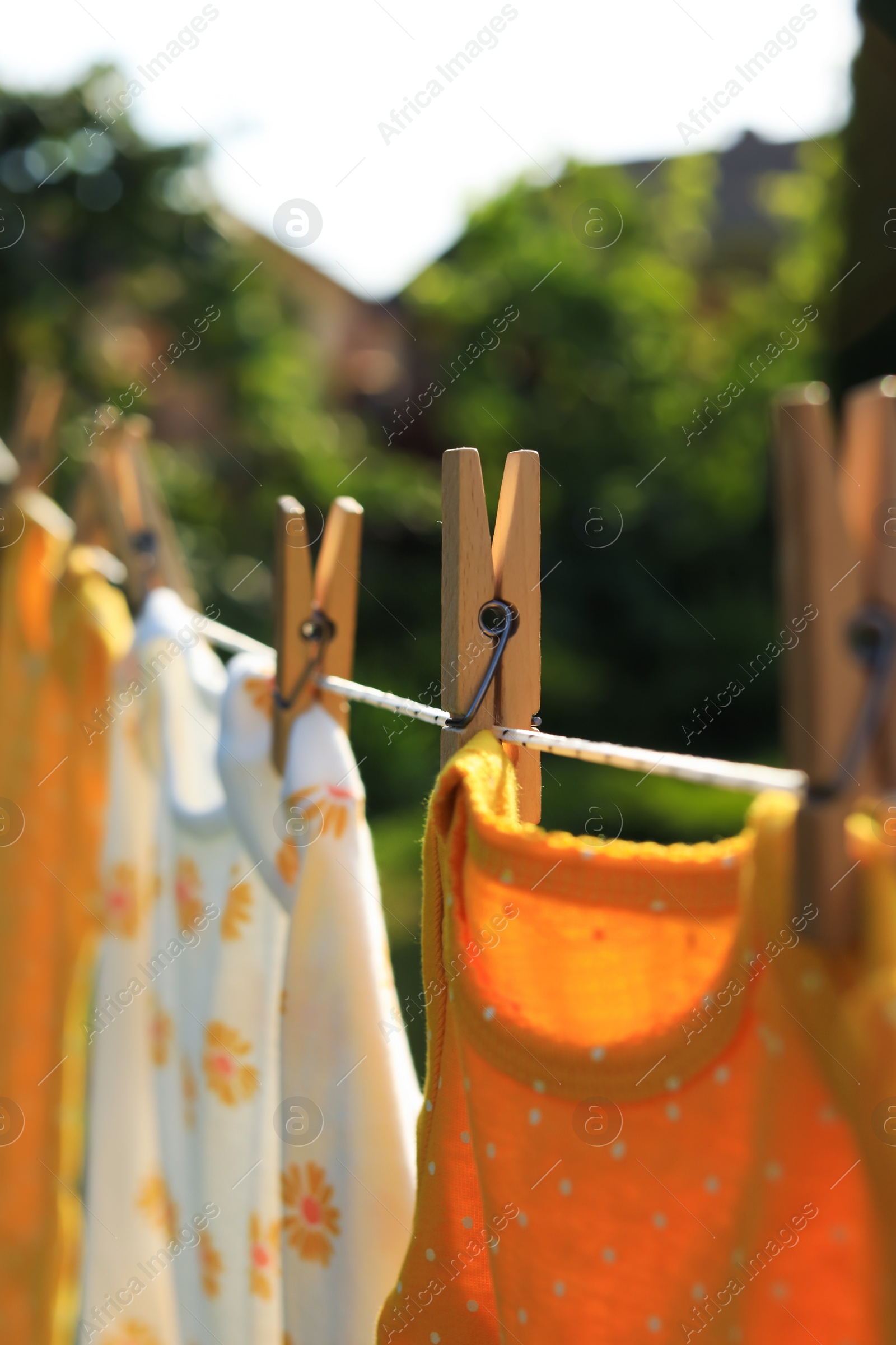 Photo of Clean baby onesies hanging on washing line in garden, closeup. Drying clothes