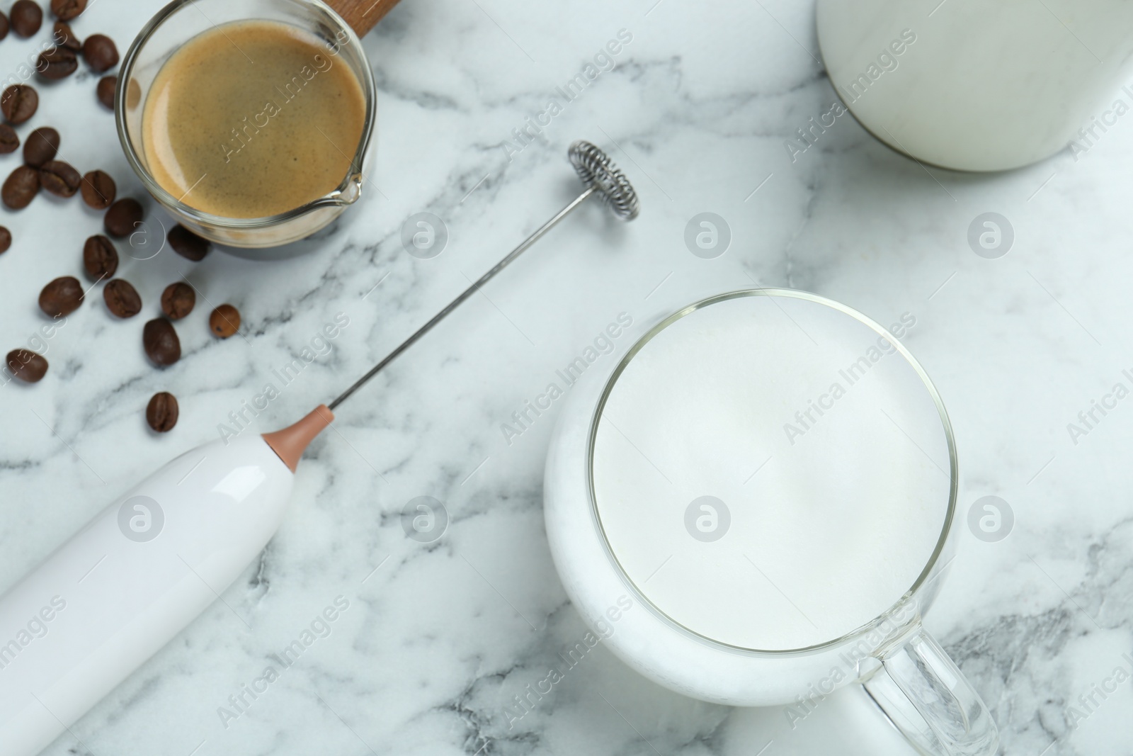 Photo of Mini mixer (milk frother), cup of milk and coffee on white marble table, flat lay