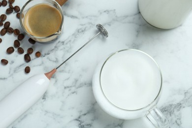 Mini mixer (milk frother), cup of milk and coffee on white marble table, flat lay