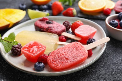 Photo of Plate of different tasty ice pops on black textured table, closeup. Fruit popsicle