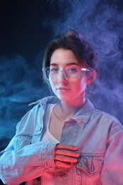 Fashionable portrait of beautiful young woman in glasses and smoke on color background