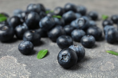 Photo of Tasty fresh blueberries and leaves on grey stone surface, closeup
