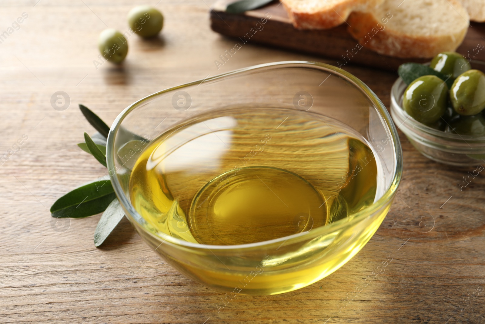 Photo of Glass bowl of olive oil on wooden table, closeup