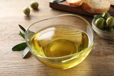 Photo of Glass bowl of olive oil on wooden table, closeup