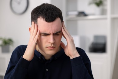 Young man suffering from headache in office, space for text