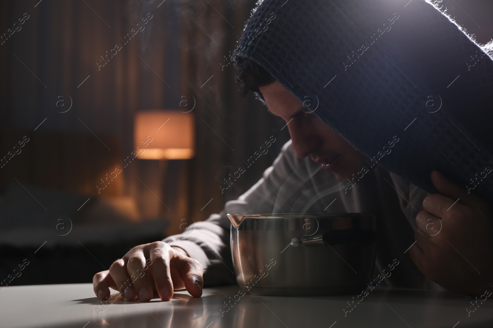 Photo of Man with plaid doing inhalation above saucepot at table indoors