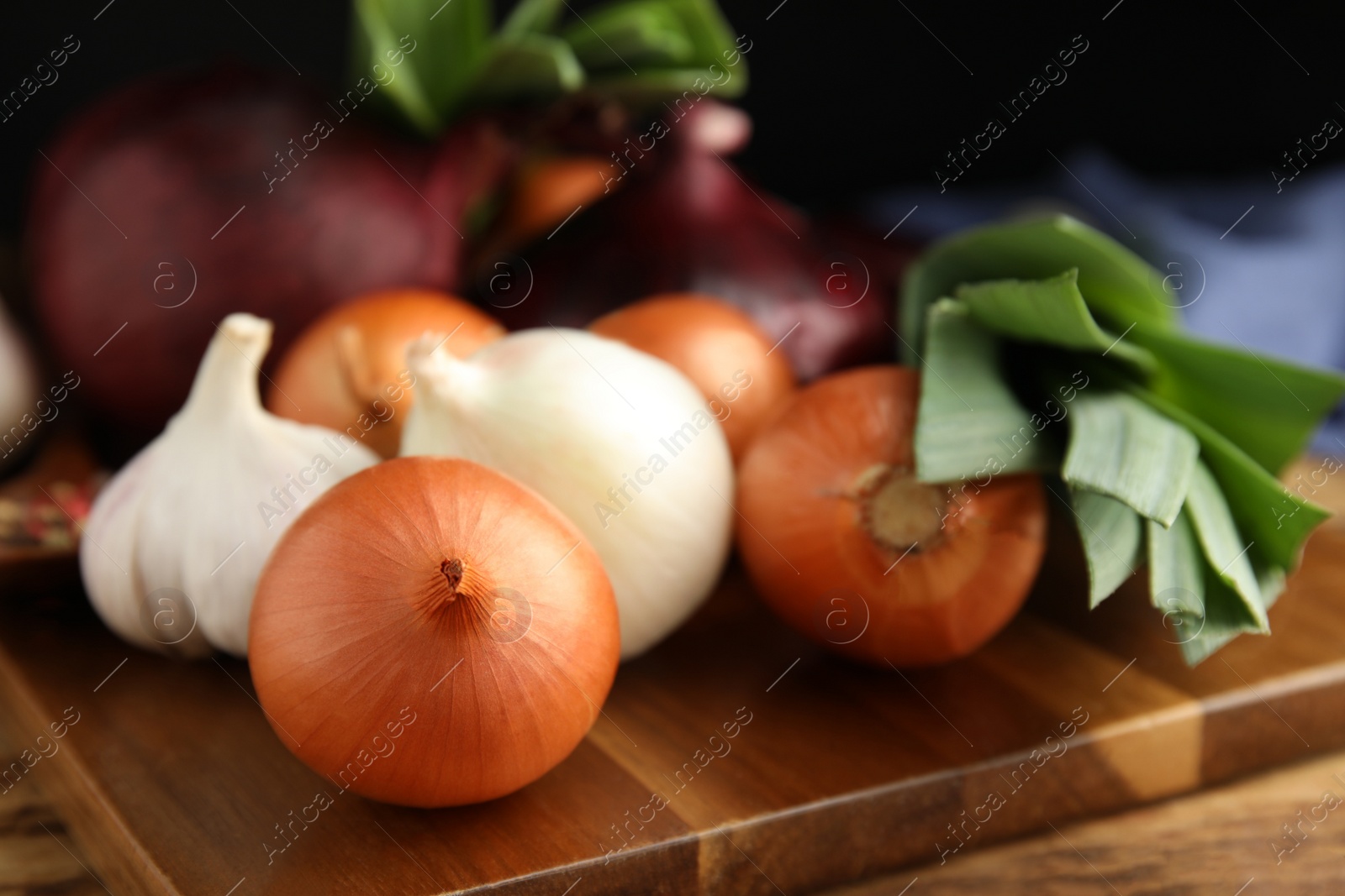 Photo of Fresh onion bulbs, leeks and garlic on wooden table, closeup