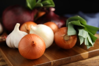 Photo of Fresh onion bulbs, leeks and garlic on wooden table, closeup