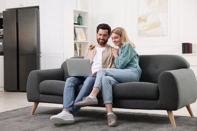 Happy couple with laptop on sofa at home