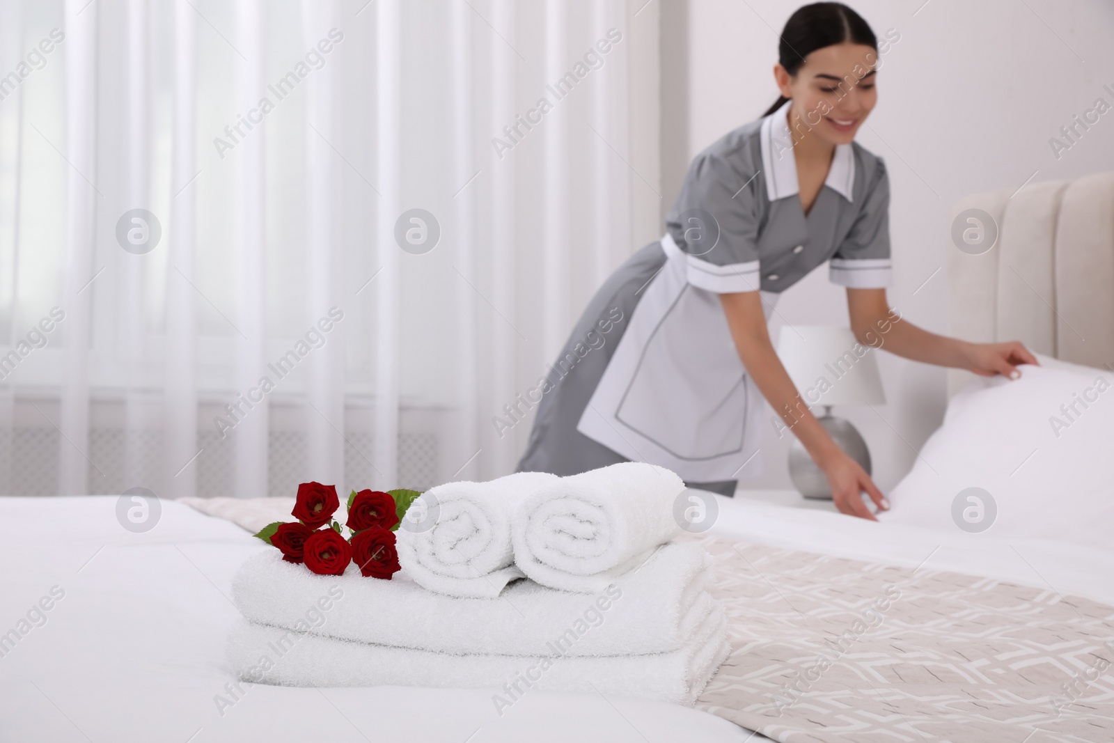 Photo of Chambermaid making bed in hotel room, focus on fresh towels. Space for text