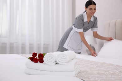 Chambermaid making bed in hotel room, focus on fresh towels. Space for text