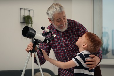 Photo of Senior man with his little grandson looking at stars through telescope in room