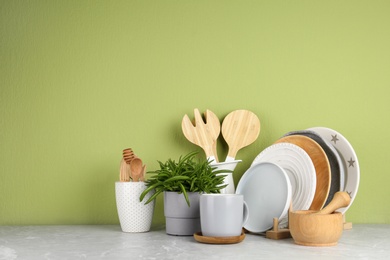 Photo of Green plant and different kitchenware on table near color wall, space for text. Modern interior design