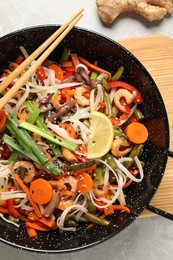 Photo of Shrimp stir fry with noodles and vegetables in wok on grey table, top view
