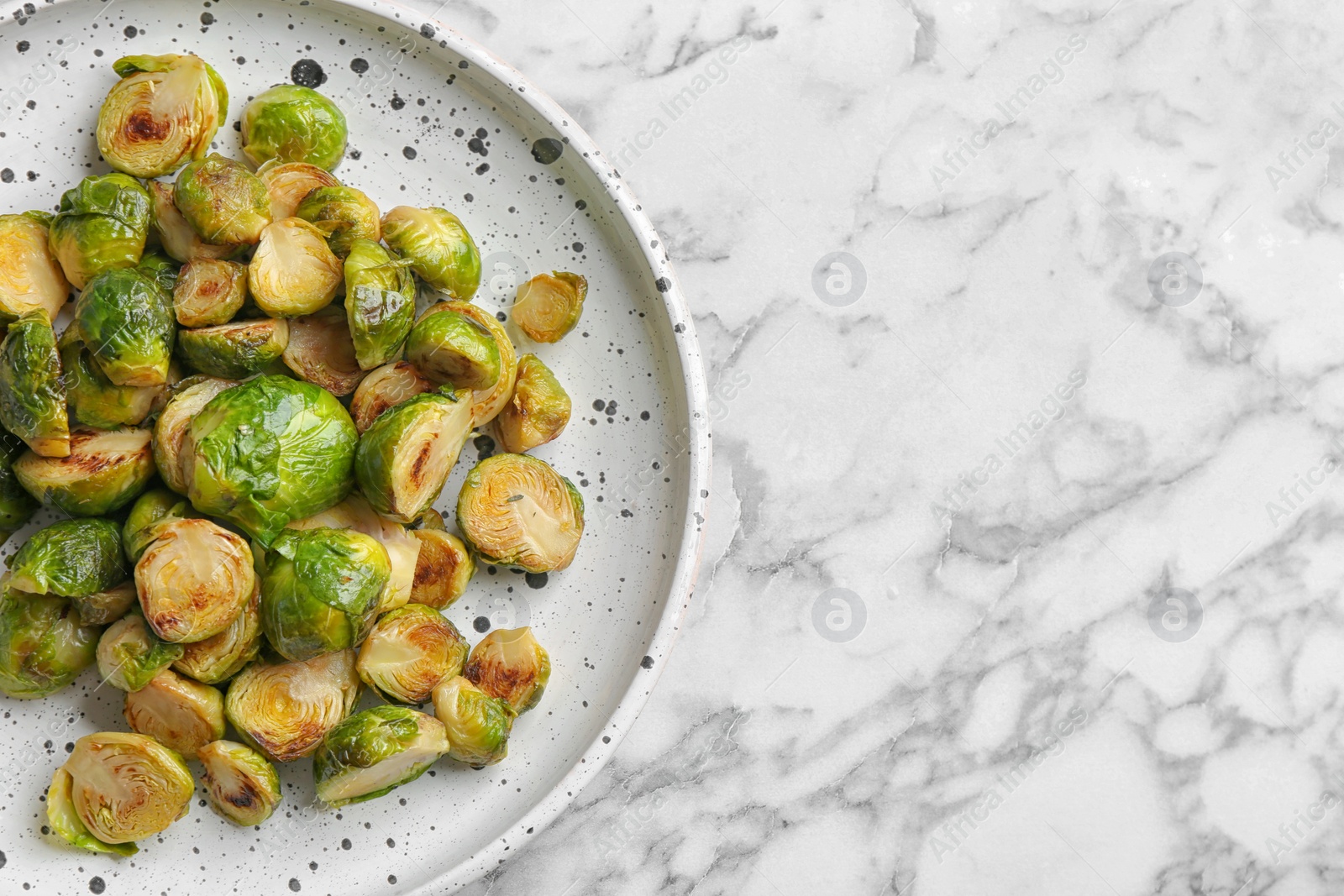 Photo of Delicious roasted brussels sprouts on white marble table, top view. Space for text