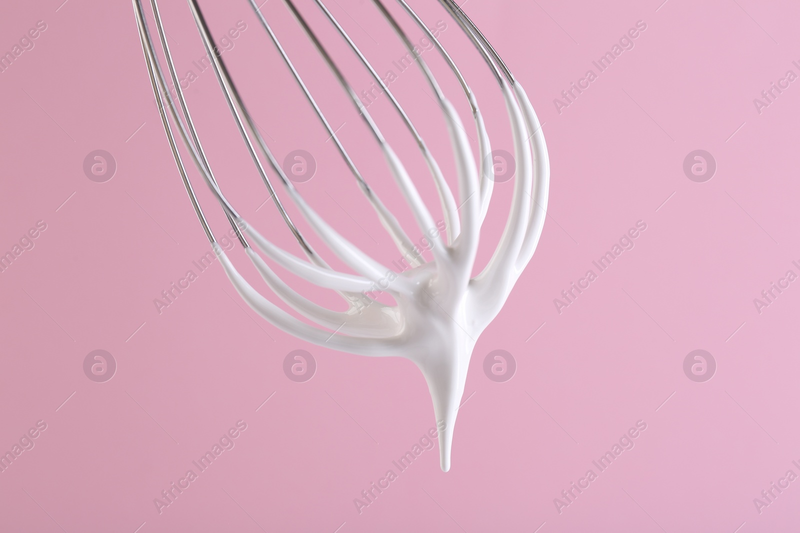 Photo of Whisk with whipped cream on pink background, closeup