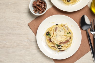 Photo of Delicious pasta with anchovies, olives and parmesan cheese served on light wooden table, flat lay. Space for text