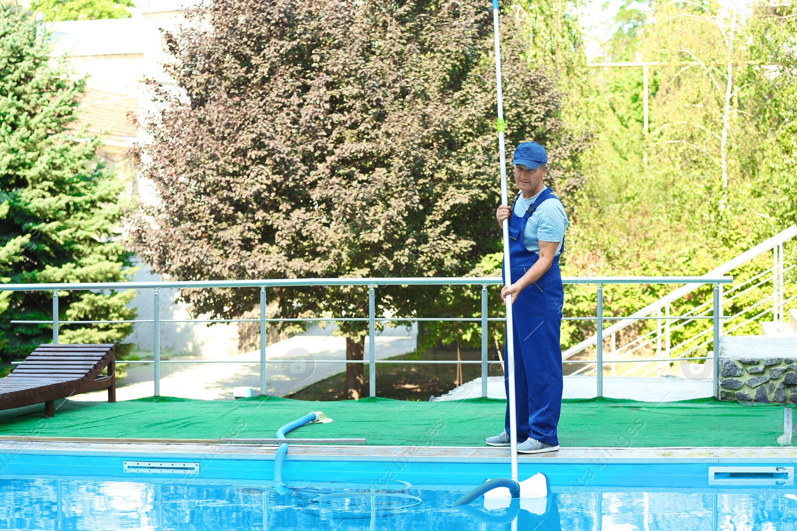 Photo of Male worker cleaning outdoor pool with underwater vacuum